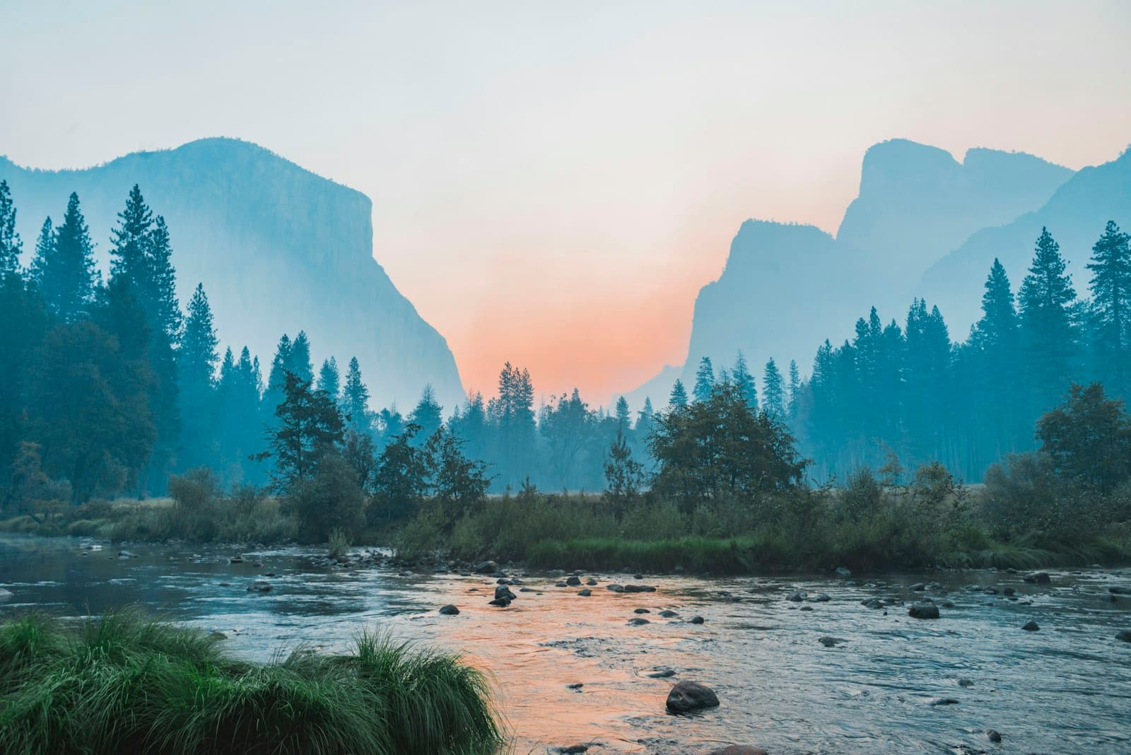 Mist settling over a river valley between forested mountains at dawn